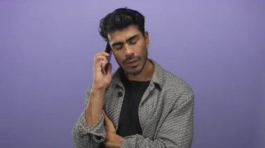 Genç İspanyol adam, stüdyo ortamında kollarını kavuşturarak akıllı telefonu kulağına tutuyor..