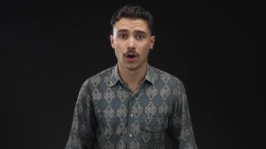 İzole edilmiş siyah arkaplan duvarına karşı duygularını ifade eden genç bir adam değişik ruh hallerinde desenli bir gömlek giyiyor dinamik ifade ve stil aktarıyor.