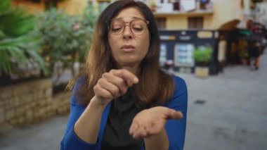 Orta yaşlı İspanyol kadın, şehir caddesinde avuç içi açık ve parmağıyla göğsü göğse gösteren hareketler yapıyor..