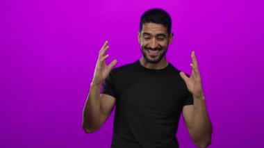 Genç adam canlı pembe bir arka plana karşı şaşkınlığını dile getiriyor, elleri başının üstünde duygularını gösteriyor, siyah bir gömlek giyiyor, İspanyol bir erkek modelin büyüleyici bir portresini yaratıyor..