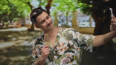 Genç adam yemyeşil bir parkta canlı bitki örtüsüyle selfie çekerken dondurmanın tadını çıkarıyor. Açık hava eğlencesi ve maceranın özünü yakalıyor..