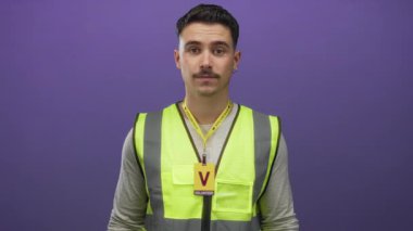 Yansıtıcı yelek giyen genç adam, izole edilmiş mor duvara karşı kamu hizmeti projesinde gönüllü olarak duruyor.