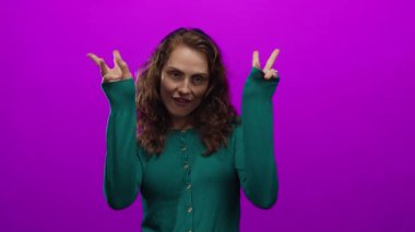 Genç bir kadın neşeli bir şekilde pembe bir arka plana karşı hareketli, kıvırcık saçlarıyla ve günlük tarzıyla duygularını ifade ediyor, tavır sergiliyor ve çevreden soyutlanıyor..