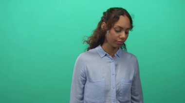 Genç bir kadın parlak bir deniz mavisi stüdyo ortamında görünür bir yüz ile aşağı bakıyor, yumuşak ışıklandırma ve nötr ifade; tefekkür.