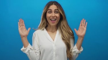 Sarışın genç bir kadın, elleri mavi stüdyo ortamında, avuçları ayrık, sürpriz sevinç coşkusu gösteriyor..