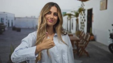 Sarışın kadın, kırsal bir avluda iki eliyle baş parmak işareti gösteriyor. Onaylama iyimserliği..