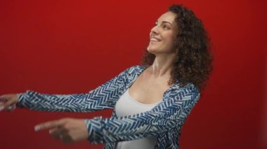 Her iki işaret parmağı yukarı doğru kırmızı bir stüdyoda gülümseyen ve hayali bir ekrana bakan, neşeli iyimserlik.