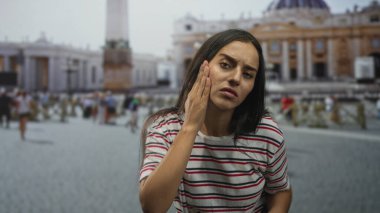 Vatikan yakınlarındaki meydanda el ele tutuşan bir kadın, endişeli görünürken halk içinde yüzünü ovuyor; cilt kaygısı.