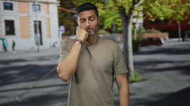 Kesilmiş sakallı ve çenesi üzerinde duran İspanyol bir adam işlek şehir caddesinde duruyor, gözleri kapalı, sessiz tefekkür.