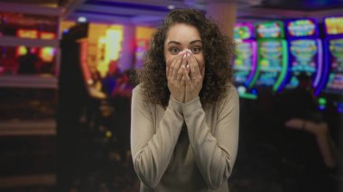 Kumarhane kumar makinesinde ağzını kapatan genç bir kadın. Şaşırmış bir ifadeyle gülümsüyor. Sürpriz şans kutlaması..