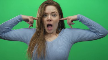 Yeşil stüdyo ortamında işaret parmaklarıyla kulakları tıkayan ve yüksek sese görünür bir tepki veren bir kadın..