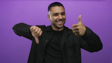 Siyah tişört giyen Latin asıllı genç adam mor stüdyo ortamında baş parmak işareti yapıyor ve kabul etmiyor..
