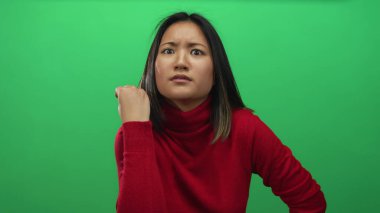 Kırmızı kazaklı genç bir kadın, yeşil bir arka plan duvarına karşı elleri ile anlamlı bir jest yapıyor. Duygularını ve dikkatini ifade ediyor..