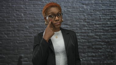 Siyah ceketli genç Afrikalı Amerikalı kadın binadaki tuğladan duvara parmak ısırıyor..