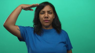 Yüzü önde olan Afro-Amerikalı kadın stüdyoda selam veriyor yeşil perde arkası ve mavi gömlekli; saygı.