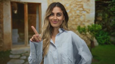 Güneşli bir bahçede yukarı doğru işaret eden neşeli genç kadın; güven pozitifliği rehberliği uyarısı.