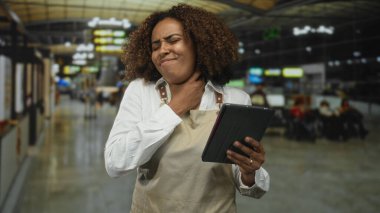Havaalanı terminalinde tablet tutarken önlüklü bir kadın boynunu tutuyor..