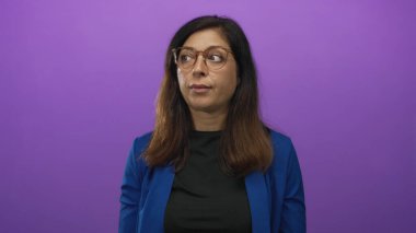 Mor stüdyoda gözlüklü ve mavi ceketli bir kadın yan bakıyor..