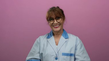 Kıdemli İspanyol kadın üniformalı, gülümseyen ve pembe arka planda öpüşen profesyonel bir ortamda sıcaklığını ve minnettarlığını ifade eden..