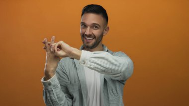 Genç adam canlı turuncu arkaplan, coşkulu ifade gösteren hashtag sembolü, kot gömlek ve beyaz tişört giyerek gündelik stil