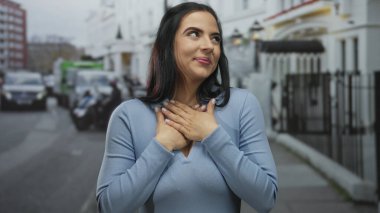Canlı bir şehir sokak ortamında modern mimari ve açık gökyüzünün altında park edilmiş arabaların karışımıyla mutlu bir şekilde gülümseyen kadın..