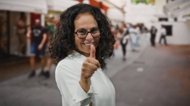 Şehrin işlek caddesinde gülümseyen ve güneşli gökyüzünün altında pozitifliği ve kıvırcık saçları vurgulayan bir kadın..