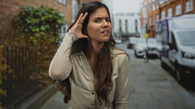 Şehir caddesinde el ele tutuşan kadın, uzak gürültüyü dinlemek için öne eğiliyor; endişe merak.