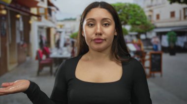 İspanyol kadın, bir sokak restoranının terasında yüzünü tarafsız bir ifadeyle gösteren kameraya bakıyor..