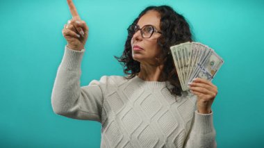 Amerikan dolarlarını elinde tutan orta yaşlı bir kadın izole edilmiş mavi bir geçmişe karşı düşünceli bir ifadeyle mali kararları ve zenginliği sembolize ediyor..