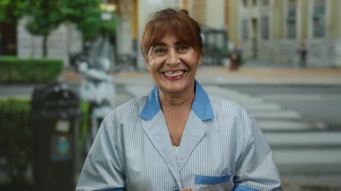 Kıdemli İspanyol kadın açık havada üniformalı bir şehir caddesinde gülümsüyor, açık havada çalışkan bir bağlılığın özünü yakalıyor..