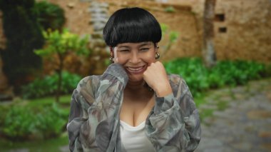 Yeşil bir parkta kadın, boks yaparken neşeli bir şekilde gülümsüyor, açık havada neşeli ve enerjik bir duygu sergiliyor..