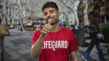 Kırmızı tişörtlü adam şehirde gündüz vakti sokakta baş parmak işareti yapıyor; güven onayı.