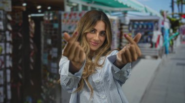 Sarışın kadın gülümsüyor ve hareketli market tezgahında kalp hareketi yapıyor; sevgi dolu neşe flörtü.