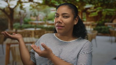 Afrika kökenli Amerikalı bir kadın, güneşli restoran binasının önünde avuçlarını kaldırırken, kafası karışmış bir ifade takınıyor..