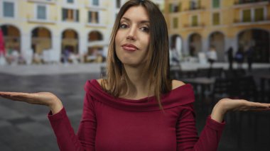 Kırmızı bluz giyen genç İspanyol kadın, kalabalık caddede bulanık kafe masalarının yanında el kol hareketi yapıyor..