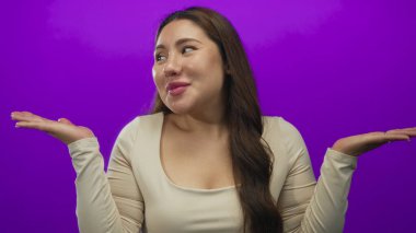 Genç İspanyol kadın omuz silker ve mor stüdyoda soru işareti olarak ellerini açık tutar; belirsizlik.