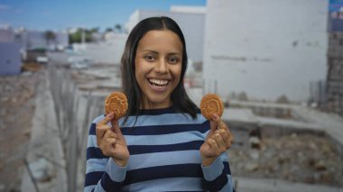 Yüzünün yanındaki kurabiyeleri tutan genç İspanyol kadın şantiyeye gülüyor. Neşeli ve neşeli çizgili bir süveter giyiyor ve enerjik bir şekilde yakalanmış..