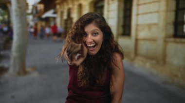 Caddedeki kamerayı işaret eden kadın bordo tişört giyiyor ve geniş bir gülümseme takınıyor. Neşeli neşeli bir kutlama..