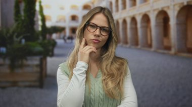 Sarışın kadın üniversite manastırında parmak uçlu yelek giyerek yanağa dokunuyor..