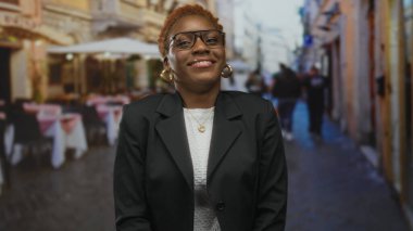 Gözlüklü ve altın küpeli bir kadın, restoranın teras masalarında gülümsüyor..