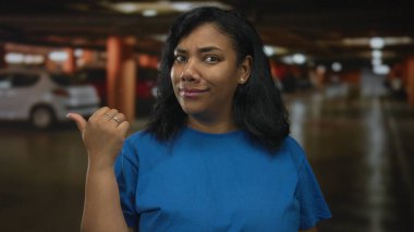 Mavi gömlekli Afro-Amerikalı kadın şüpheli bir ifadeyle arabayı işaret ediyor..