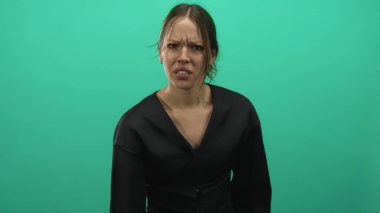 İspanyol kadın sıkılmış yumruğunu kaldırıyor ve stüdyonun yeşil arka planında suratını buruşturuyor..