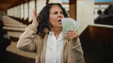 Üniversitede orta yaşlı bir kadın elinde Singapur banknotları tutarken akademik ortamda maddi stresin göstergesi olarak acı dolu bir ifade kullanıyordu..