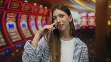 Genç kadın, parlak ışıklar altında stüdyoda kumar makinesinin yanında burnunu sıkar ve sırıtır..
