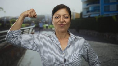 Rıhtımın yanındaki modern binanın önünde kol kaslarını esneten kadın, kendine güven güçlendirici..