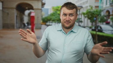 Şehirdeki binaların ve park edilmiş arabaların yakınındaki bir caddede avuçlarıyla omuz silken şişman genç bir adam..
