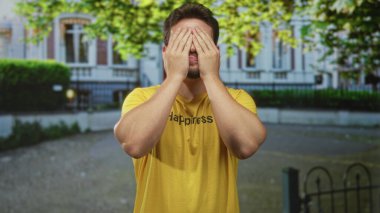 Binaların önünde mutluluğu okuyan sarı tişört giyen gözleri kaplayan adam neşeli bir oyunculuk sergiliyor..