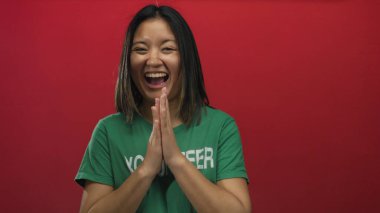 Yeşil tişörtlü bir kadın kırmızı arkaplanda el çırpıyor neşeli gönüllü ruhunu ifade ediyor gençlik enerjisi ve coşkusu sergiliyor..