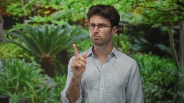 Gözlüklü bir adam ve çenesinde eli çizgili bir gömlek ve açık havada gür bir ormanda parmakla göstermek; düşünceli yansıma.