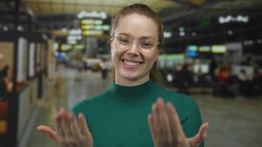 Yeşil balıkçı yaka kazaklı gülümseyen kadın yoğun havaalanı terminalinde ellerini sıktı; dinginlik iyimserliği iyimserliği.